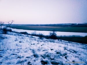 Замёрзла река, протекающая мимо Воскресенска, пригорода Николаева. Также на фото видно камыши и снег. На дворе сумерки.