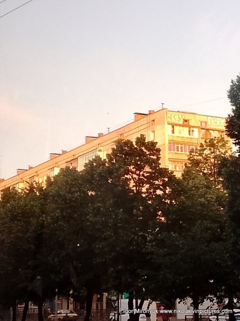 На фото видно золотистое здание с алеей зелёных деревьев. "Золотистое" - потому что в свете солнца на горизонте.