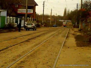 Улица в Николаеве с грунтовой, неасфальтированной дорогой и проложенными на ней трамвайными рельсами и едущим по ним трамваем.